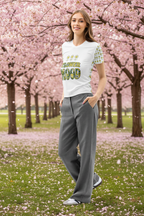 Woman standing in a cherry blossom garden wearing a white t-shirt with text and gray pants.