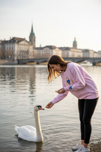 Woman feeding a swan on a lake with a cityscape in the background