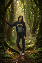 Woman standing in a forest wearing a black sweatshirt with colorful design