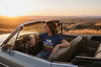 Woman sitting in a convertible car with a scenic background during sunset.