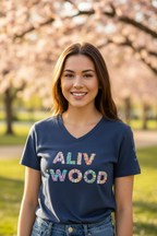 Woman wearing a blue t-shirt with 'ALIV WOOD' printed on it, standing in a park with cherry blossom trees.